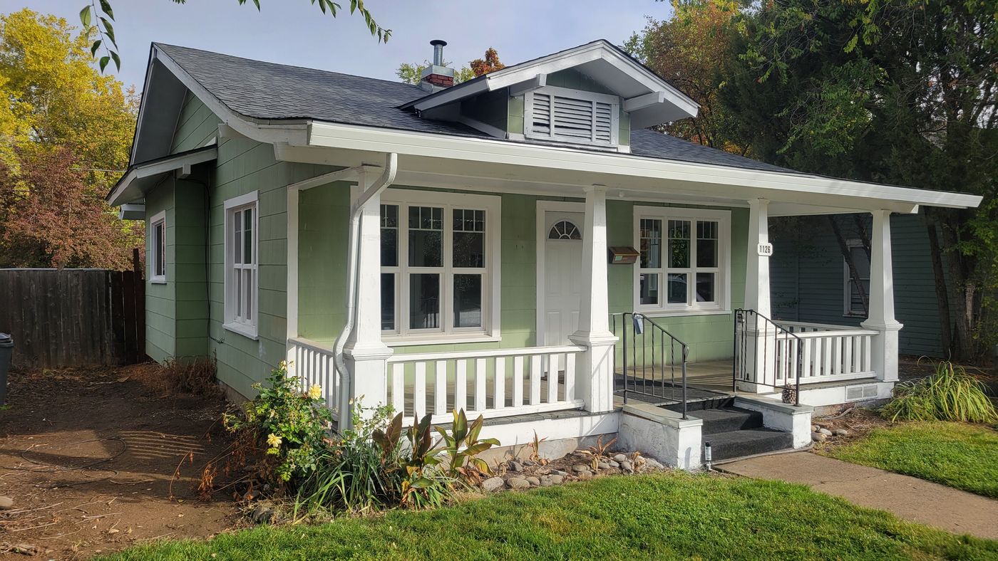 Front corner of the green Medford house with garden beds along the porch