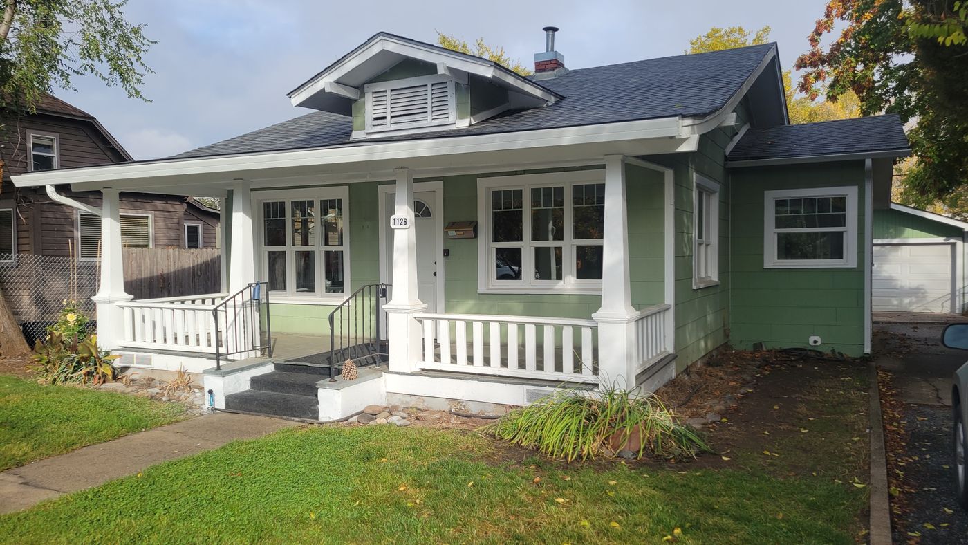 Covered front porch with white columns and railings on the green Medford house